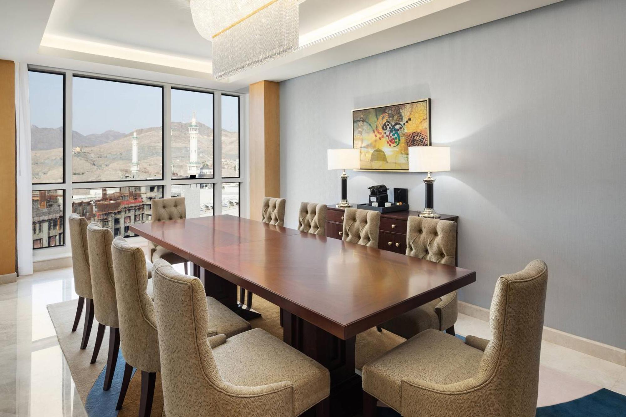 Sheraton Makkah Jabal Al Kaaba Hotel Мекка Экстерьер фото The photo shows a modern conference room with a large wooden table surrounded by upholstered chairs. The room is well-lit, featuring large windows that offer a view of the outdoors, possibly with mountains in the background. On one wall, there is a p
